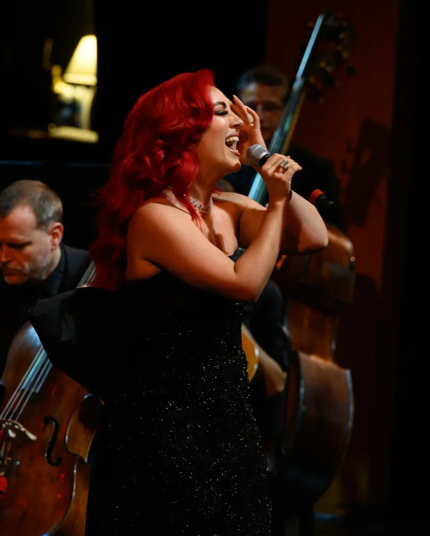 Monique Abbadie singing into the microphone with the orchestra positioned behind her.