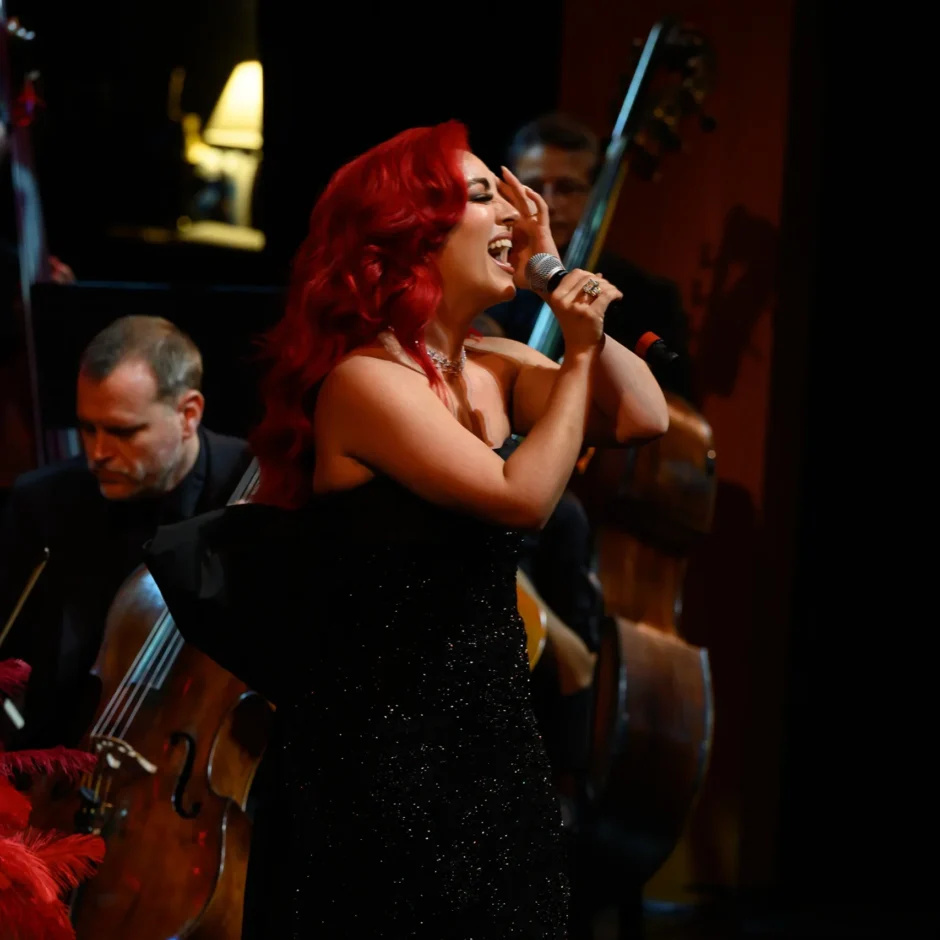 Monique Abbadie singing into the microphone with the orchestra positioned behind her.