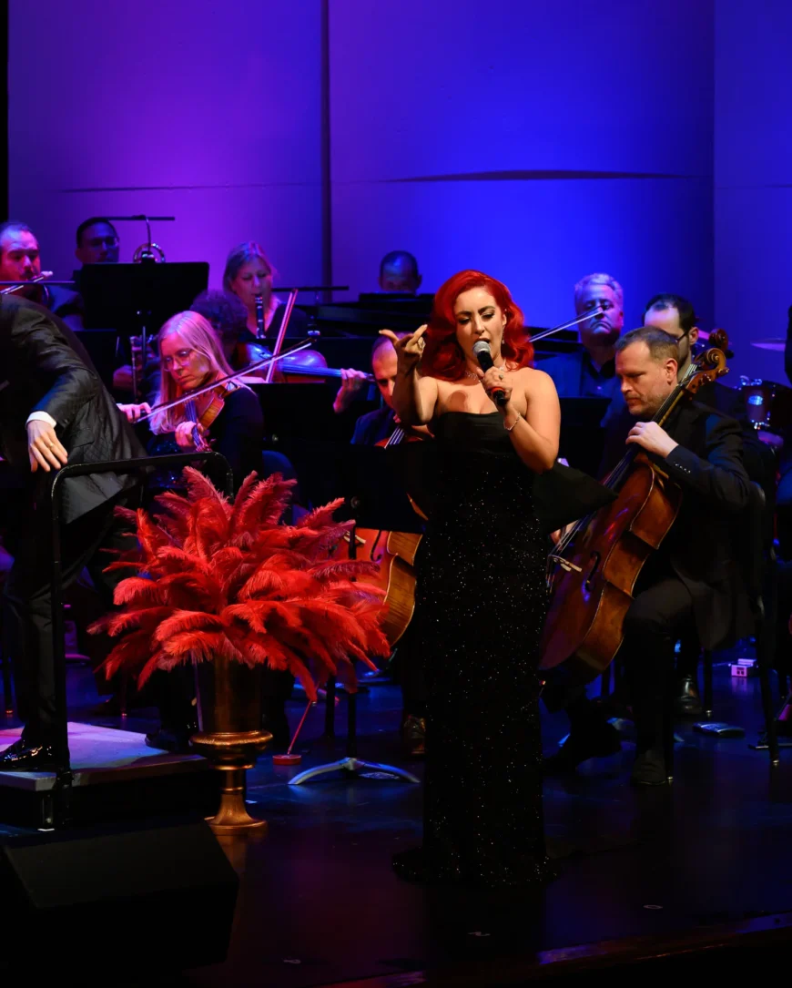 Monique Abbadie singing onstage with the orchestra visible behind her.