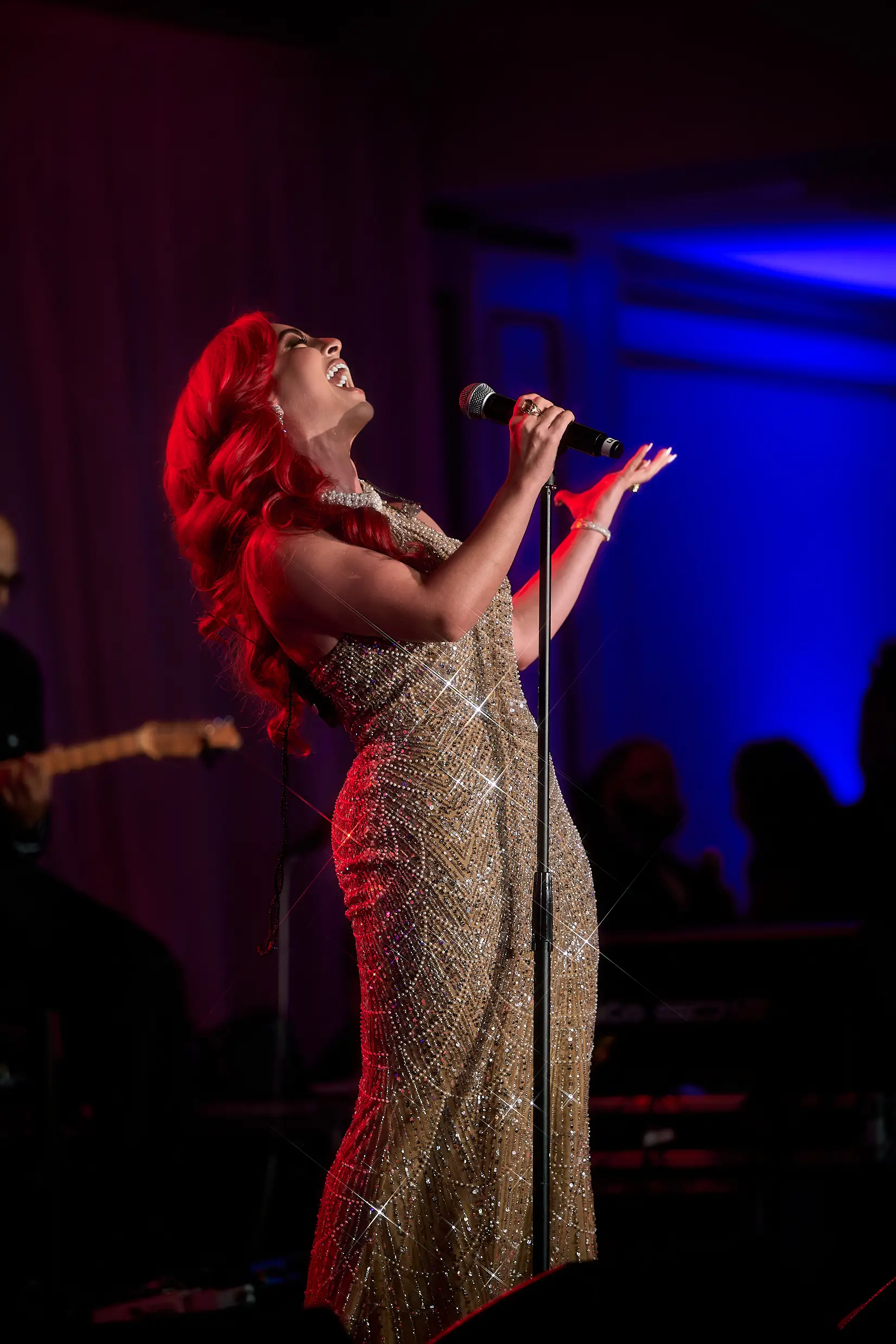 Monique Abbadie singing in a golden gown under red stage lighting at the Whitney E. Houston Foundation gala