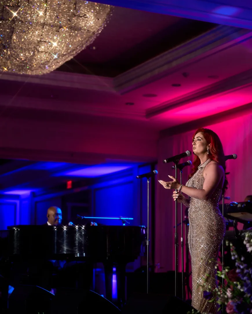 Monique Abbadie singing beside a grand piano at the Whitney E. Houston Foundation gala